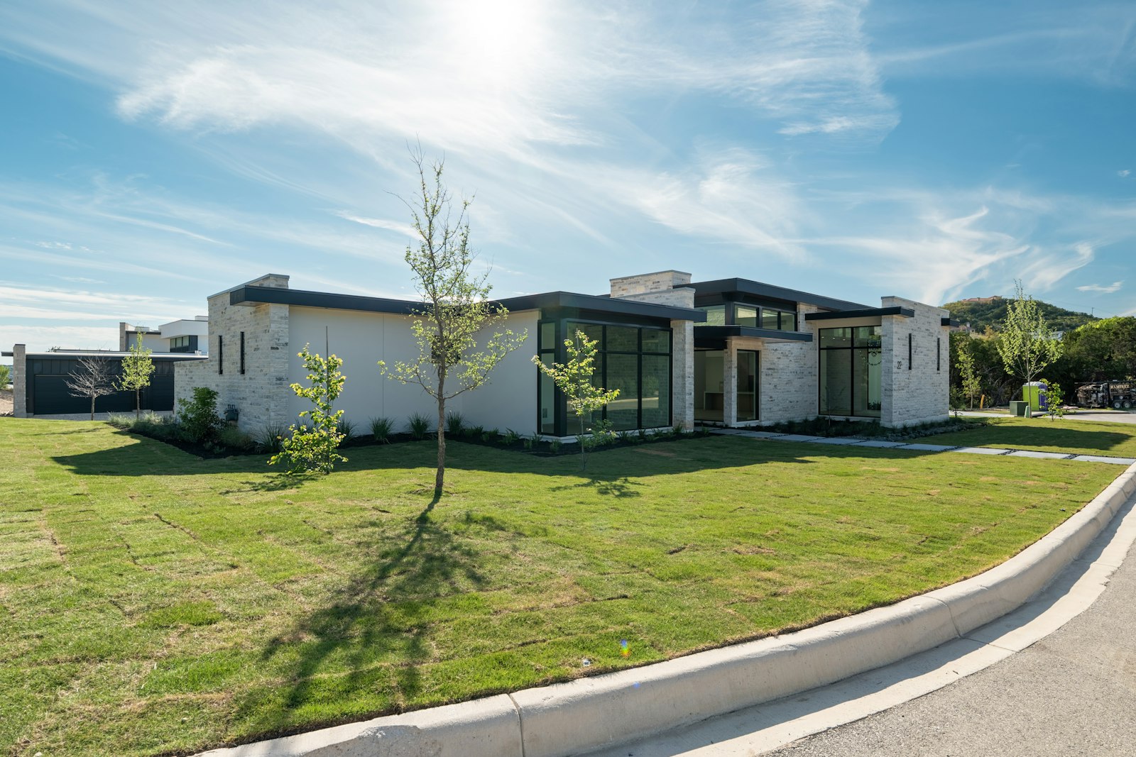 A modern single-story stone-and-stucco home on a wide green lawn under a clear blue sky