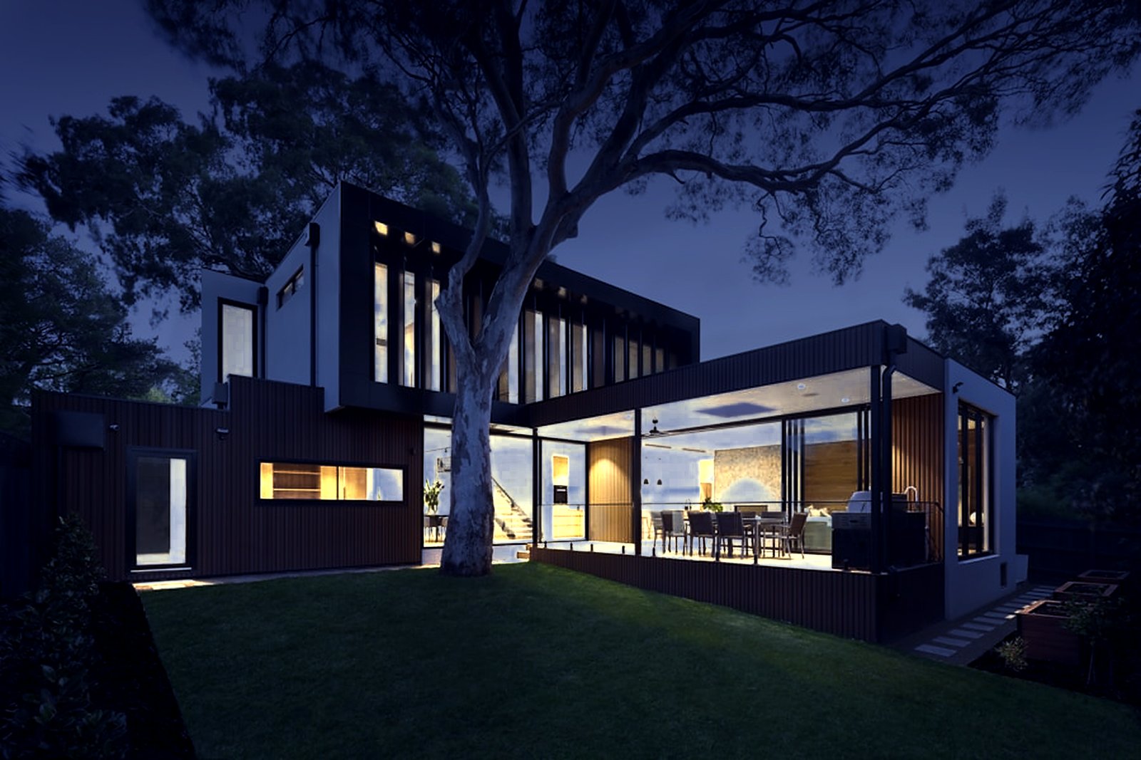 A modern timber-clad home at night, the only warm light on the street coming from inside